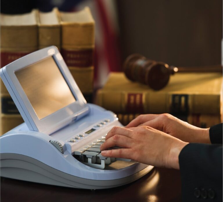 A person is typing on a stenotype machine, with a few law books and gavel in the background.