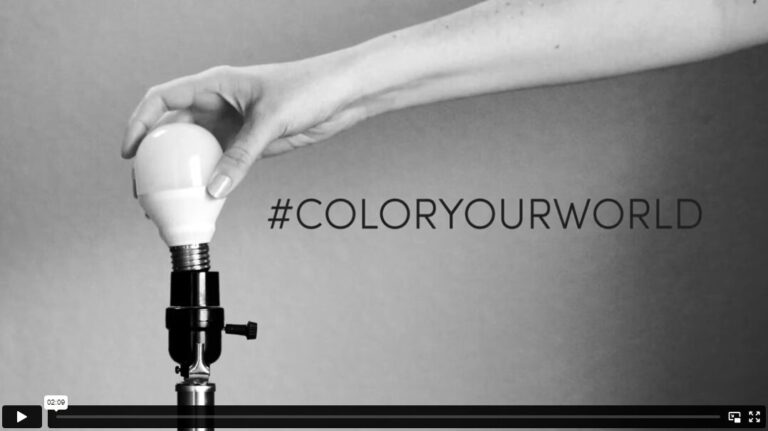 Thumbnail of a video shows a black and white image of a hand screwing in a lightbulb on a lamp. To the right is a hashtag that reads “#ColorYourWorld”.